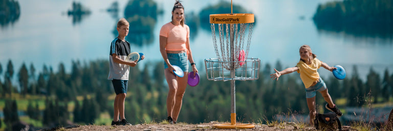 En familie med en mor og to børn der spiller disc golf med havet i baggrunden